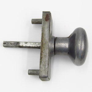 Könnte beinhalten: Ein silberner Türknauf mit einem runden Griff und einer quadratischen Basis. Der Knauf hat ein Schlüsselloch und eine kleine Metallstange, die sich von der Basis erstreckt.