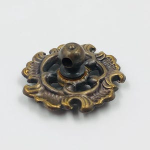May include: An antique brass drawer pull with an elaborate floral design. The pull has a round knob and a detailed, aged finish. Suitable for vintage furniture restoration projects.