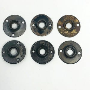 Könnte beinhalten: Sechs antike, kreisförmige Metallbeschläge für Türen. Jedes Teil hat ein zentrales Loch und drei kleinere Löcher am Umfang. Das Metall hat ein abgenutztes, gealtertes Aussehen mit Farbvariationen, die von Dunkelbraun bis Bronze reichen.
