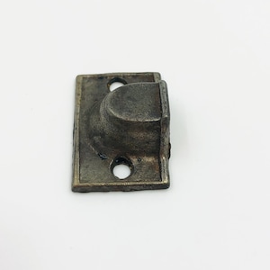 May include: A small, antique-style metal door pull with a rectangular base and a curved, rounded handle. The hardware is a tarnished, aged bronze color, with two screw holes visible.