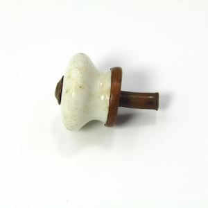 May include: A vintage white ceramic cabinet knob with a brown metal base and stem. The knob has a rounded shape with a slightly aged appearance, suggesting it is an antique or a reproduction. The metal components show signs of wear.