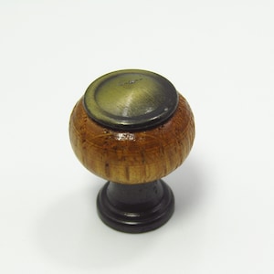 May include: A wooden cabinet knob with a round, textured body and a dark bronze-colored top. The base is a dark brown color. The knob is designed for furniture and has a classic, timeless look.