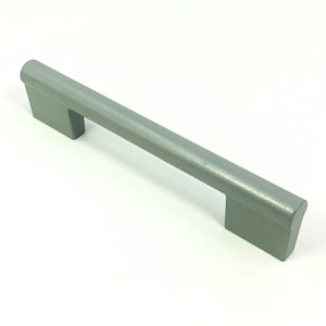 Puede incluir: Un tirador de armario de color plateado. El tirador es rectangular con bordes redondeados y una barra recta. El tirador mide aproximadamente 15 cm de largo y está hecho de metal. El tirador está diseñado para armarios y cajones.
