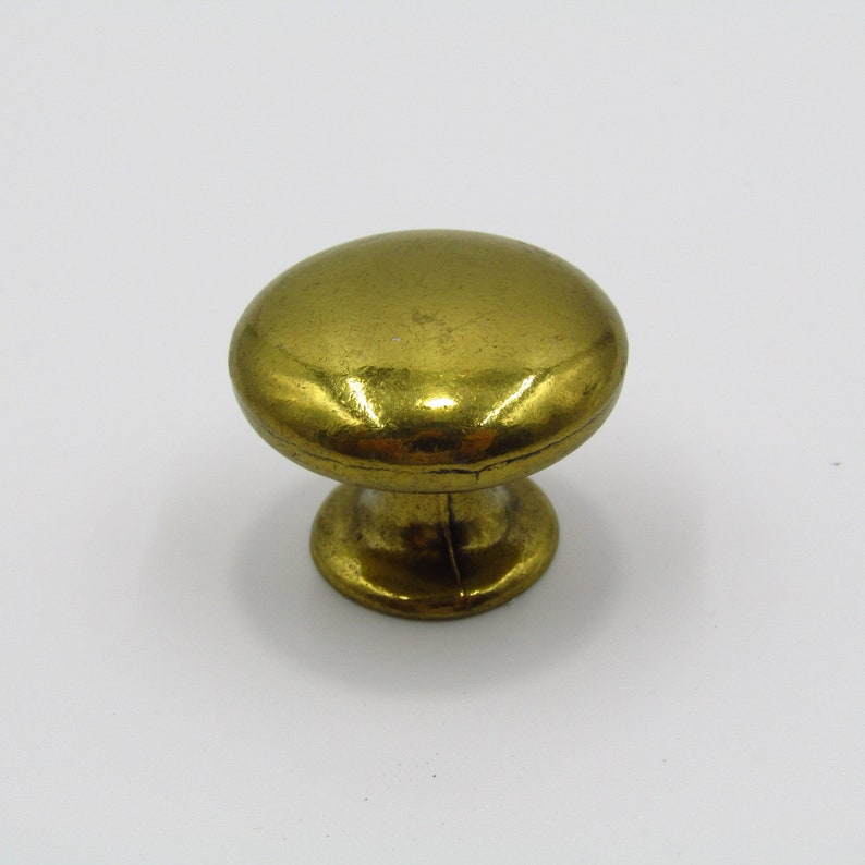 Puede incluir: Un pomo de armario de metal dorado con la parte superior redonda y una base ligeramente elevada.