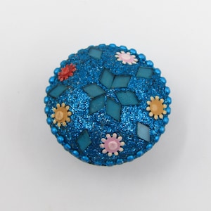 Puede incluir: Un adorno redondo, azul, brillante con un patrón de mosaico y detalles de flores de colores.