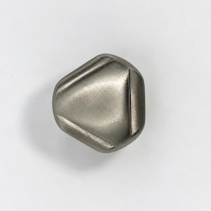 May include: A brushed silver-toned metal cabinet knob with a rounded triangular shape. The surface features a smooth, matte finish with three distinct recessed lines that form a triangle pattern across the center of the knob face.