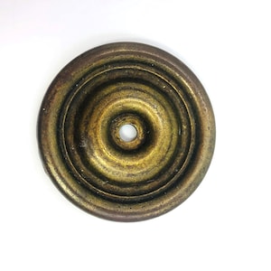May include: A circular, antique brass-toned metal object with concentric rings and a central hole. The object has a weathered appearance, with variations in color from gold to dark brown.