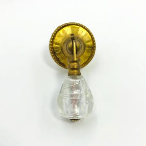 Op de afbeelding: Antieke messing ladeknop met een heldere, facetgeslepen glazen druppelvormige handgreep. De messing achterplaat is rond met een parelrand. Een vintage-stijl meubelbeslag.