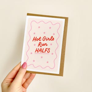 May include: A greeting card with a brown border and a light pink background. The card features the text "Hot Girls Run Halfs" in red, with pink stars and a wavy pink border.