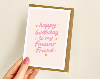 May include: A birthday greeting card with a light pink background and the text "happy birthday to my Forever Friend" in pink script. The card is in a brown envelope and has small yellow star accents.