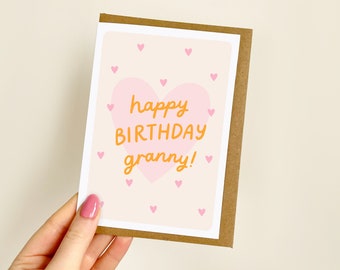 May include: A birthday card with a brown border and a pale pink background. The card has a large pink heart with the words "happy BIRTHDAY granny!" in orange. Small pink hearts are scattered around the card.