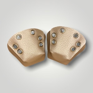 May include: A pair of tan-coloured shoe protectors made from a leather-like material. Each has a textured surface and six gold-coloured eyelets. These protectors are designed to shield the front of shoes.