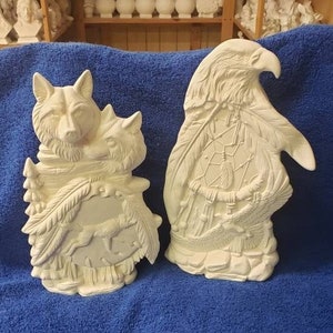 K&ouml;nnte beinhalten: Zwei Keramikfiguren, eine von einem Wolf und die andere von einem Adler, beide mit aufwendigen Details und einer wei&szlig;en Oberfl&auml;che. Die Wolfsfigur h&auml;lt einen kleineren Wolf in seinen Pfoten, und die Adlerfigur hat ein Traumf&auml;nger-Design auf der Brust.