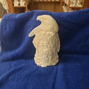 K&ouml;nnte beinhalten: Wei&szlig;e Keramikfigur eines Adlers, der auf einem Baumstumpf sitzt. Der Adler blickt nach links und hat seine Fl&uuml;gel ausgebreitet. Der Baumstumpf ist texturiert, um wie Rinde auszusehen.