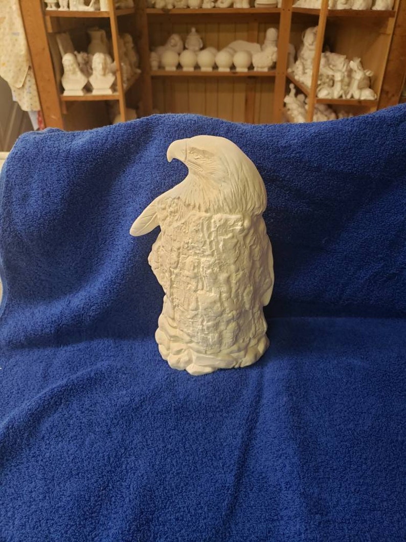 K&ouml;nnte beinhalten: Wei&szlig;e Keramikfigur eines Adlers, der auf einem Baumstumpf sitzt. Der Adler blickt nach links und hat seine Fl&uuml;gel ausgebreitet. Der Baumstumpf ist texturiert, um wie Rinde auszusehen.