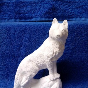May include: White ceramic figurine of a wolf standing on a rock. The wolf is facing forward with its head tilted slightly up. The figurine is unpainted and ready to be decorated.