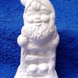 May include: White ceramic gnome figurine with a smiling face and a beard. The gnome is sitting on a ladder with his hands on the rungs.