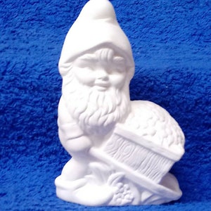 May include: White ceramic gnome figurine holding a wheelbarrow filled with small round objects. The gnome has a beard and a pointed hat.