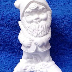 May include: White ceramic gnome figurine with a beard and a hat. The gnome is holding a small object in its hands.