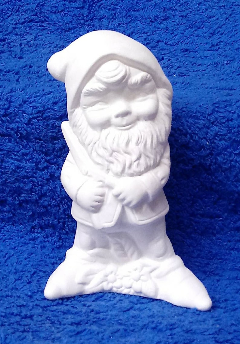 May include: White ceramic gnome figurine with a beard and a hat. The gnome is holding a small object in its hands.