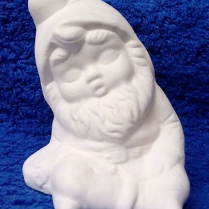 May include: White ceramic gnome figurine with a rounded hat, closed eyes, and a beard. The gnome is sitting with its legs crossed and its hands resting on its lap.