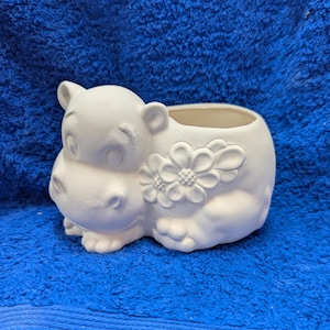 May include: White ceramic planter shaped like a hippopotamus with a flower design. The planter has a wide opening for planting.