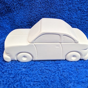 May include: White ceramic car shaped piggy bank. The car has a simple design with rounded edges and no visible details.