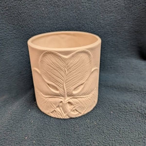 May include: A white ceramic planter with a raised design of a leaf. The planter is cylindrical and has a smooth, matte finish.