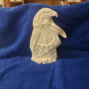 K&ouml;nnte beinhalten: Wei&szlig;e Keramikfigur eines Adlers mit einem Traumf&auml;nger in seinen Krallen. Der Adler blickt nach rechts und hat seine Fl&uuml;gel ausgebreitet. Der Traumf&auml;nger besteht aus Federn und Perlen.