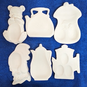 May include: Six white ceramic teapot-shaped dish sets. The dishes are in various shapes, including a bear, a teapot, a house, and a bird. The dishes are all blank and ready to be painted.