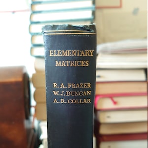 Może przedstawiać: Czarna książka w twardej oprawie zatytułowana "Elementary Matrices" autorstwa R.A. Frazera, W.J. Duncana i A.R. Collara.