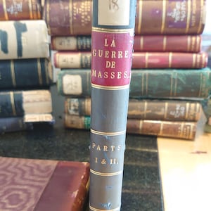 May include: A vintage book titled "La Guerre de Masses" with gold lettering on a red spine. The book is labeled "Parts I & II" and "Staff College" on the spine. The book is labeled "K 18" on the front cover.