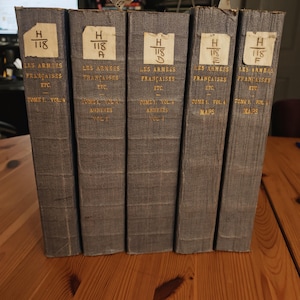 May include: A collection of five vintage books with gray covers. Each book has a label with the text "H 118" and French text. The books are standing upright on a wooden surface. The spines of the books are visible.