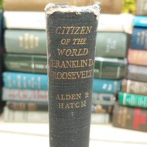 May include: A close-up of a vintage book titled "Citizen of the World" by Franklin D. Roosevelt, written by Alden B. Hatch. The book has a dark cover with gold lettering and is part of a stack of books.