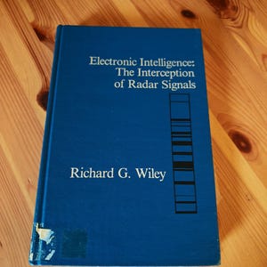 Può includere: Un libro con copertina rigida blu intitolato Electronic Intelligence: The Interception of Radar Signals di Richard G. Wiley. La copertina presenta testo bianco e un grafico nero di linee orizzontali. C'è una leggera usura nell'angolo in basso a sinistra.