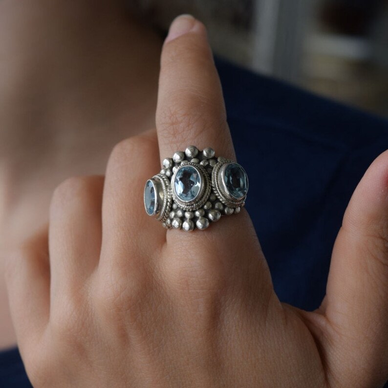 May include: A silver ring with three oval-shaped blue gemstones set in a decorative silver band.