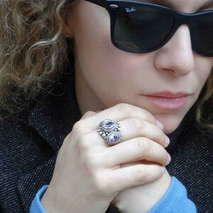 May include: A silver ring with two oval-shaped amethyst gemstones set in a beaded design.