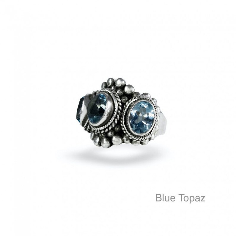 May include: A silver ring with three blue topaz gemstones set in a decorative design.