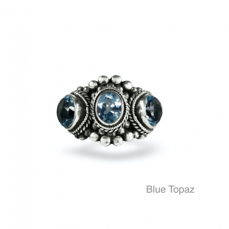 May include: A silver ring with three blue topaz gemstones set in a decorative design.