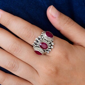May include: A silver ring with three oval-shaped ruby gemstones set in a beaded design.