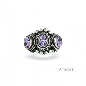 May include: A silver ring with three amethyst gemstones set in a detailed design. The ring has a beaded border and a textured surface.
