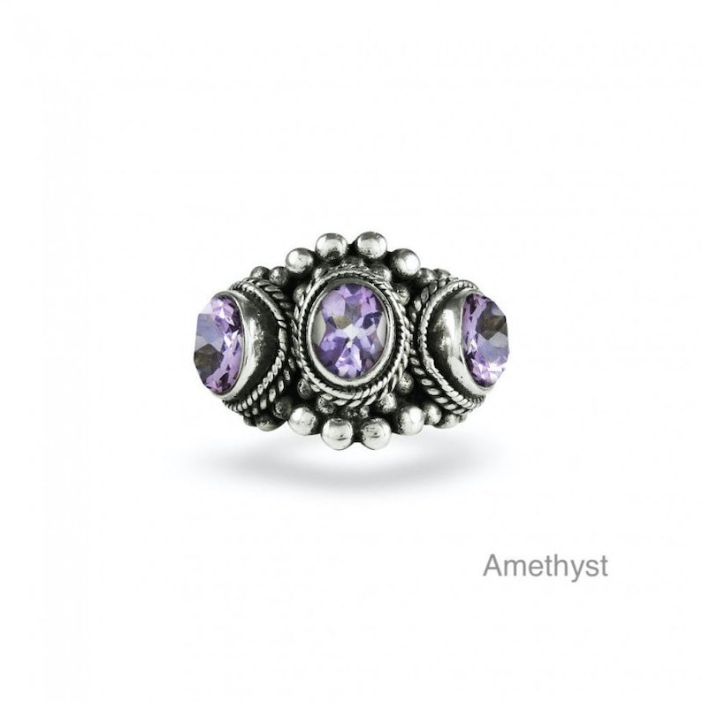 May include: A silver ring with three amethyst gemstones set in a detailed design. The ring has a beaded border and a textured surface.