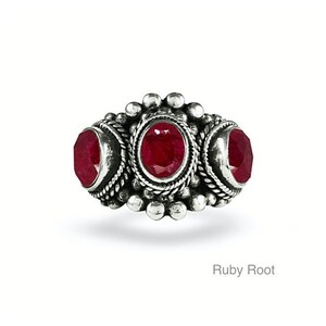May include: A silver ring with three red ruby stones set in a decorative design. The ring is called "Ruby Root".
