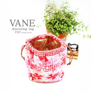 K&ouml;nnte beinhalten: Ein handgefertigter Kordelzugbeutel mit Patchwork-Design in Rot-, Rosa- und Wei&szlig;t&ouml;nen. Die Tasche hat ein rot-wei&szlig; kariertes Muster an der Oberseite und einen braunen Kordelverschluss. Der Text "VANE drawstring bag PDF sewing pattern" ist sichtbar.