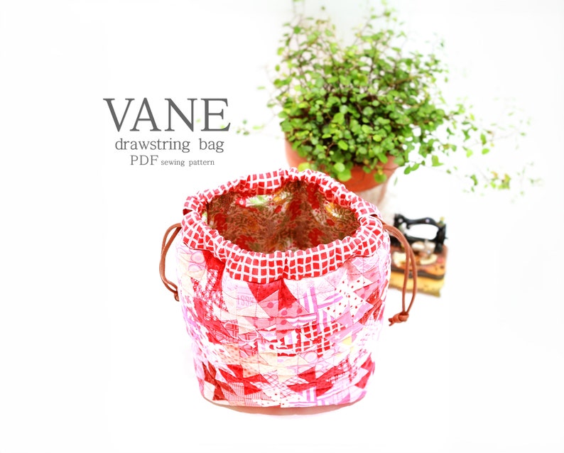 K&ouml;nnte beinhalten: Ein handgefertigter Kordelzugbeutel mit Patchwork-Design in Rot-, Rosa- und Wei&szlig;t&ouml;nen. Die Tasche hat ein rot-wei&szlig; kariertes Muster an der Oberseite und einen braunen Kordelverschluss. Der Text "VANE drawstring bag PDF sewing pattern" ist sichtbar.