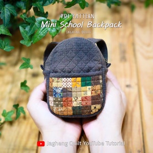 Puede incluir: Una pequeña mochila acolchada marrón con un bolsillo de tela de patchwork. La mochila está siendo sostenida en dos manos. El texto "PDF PATTERN Mini School Backpack" está en la parte superior de la imagen. El texto "Jagheung Quilt YouTube Tutorial" está en la parte inferior de la imagen.