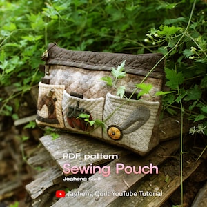 May include: A brown quilted sewing pouch with multiple pockets and a zipper closure. The pouch is decorated with fabric appliques of a sewing machine, a pumpkin, and a heart. The text "PDF pattern Sewing Pouch Jagheung Quilt" is printed on a wooden surface below the pouch. The text "Jagheung Quilt YouTube Tutorial" is printed below the first text.
