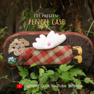 May include: PDF pattern for a pencil case shaped like a brown and red patchwork angel with a white wing and a pink star. The text "PDF PATTERN PENCIL CASE JAGHENG QUILT" is at the top of the image. The text "Jagheng Quilt YouTube Tutorial" is at the bottom of the image.