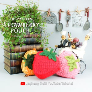 May include: PDF pattern for a strawberry pouch. The image shows three pouches: a red strawberry pouch, a pink strawberry pouch, and an orange pumpkin pouch. The pouches are made of felt and have a quilted texture. The image also includes a stack of books, a green plant, and a figurine of two chefs riding a bicycle.