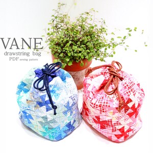 K&ouml;nnte beinhalten: Zwei Patchwork-Kordelzugbeutel, einer blau und einer rot, mit dem Text "VANE drawstring bag PDF sewing pattern". Die Beutel bestehen aus kleinen, geometrischen Stoffst&uuml;cken und haben Kordelverschl&uuml;sse. Eine kleine Topfpflanze befindet sich im Hintergrund.